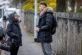 Two young people are facing each other on the street, talking about bad sex. Both are wearing black puffer jackets with hoods