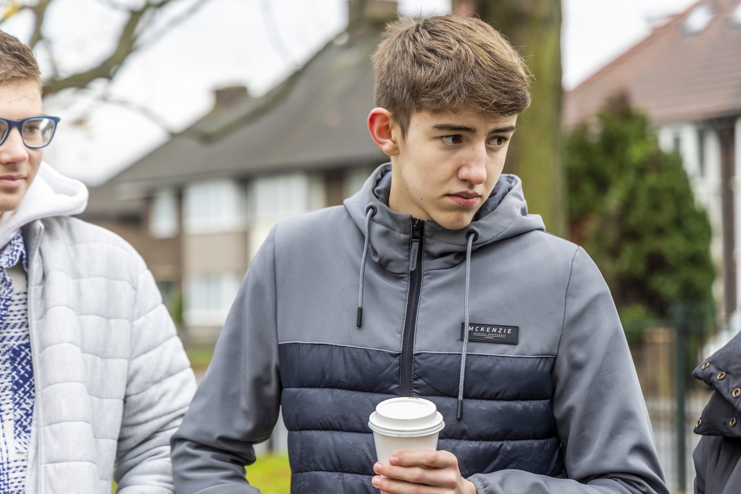 A young person is standing outside holding a coffee to cope with the effects of the morning after a night of partying