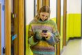 A young person is standing in a corridor wearing a rainbow striped jumper. They are looking at their phone to find out how to know if you've got hepatitis B