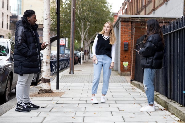 Three young people are standing around in the street, talking about cystitis