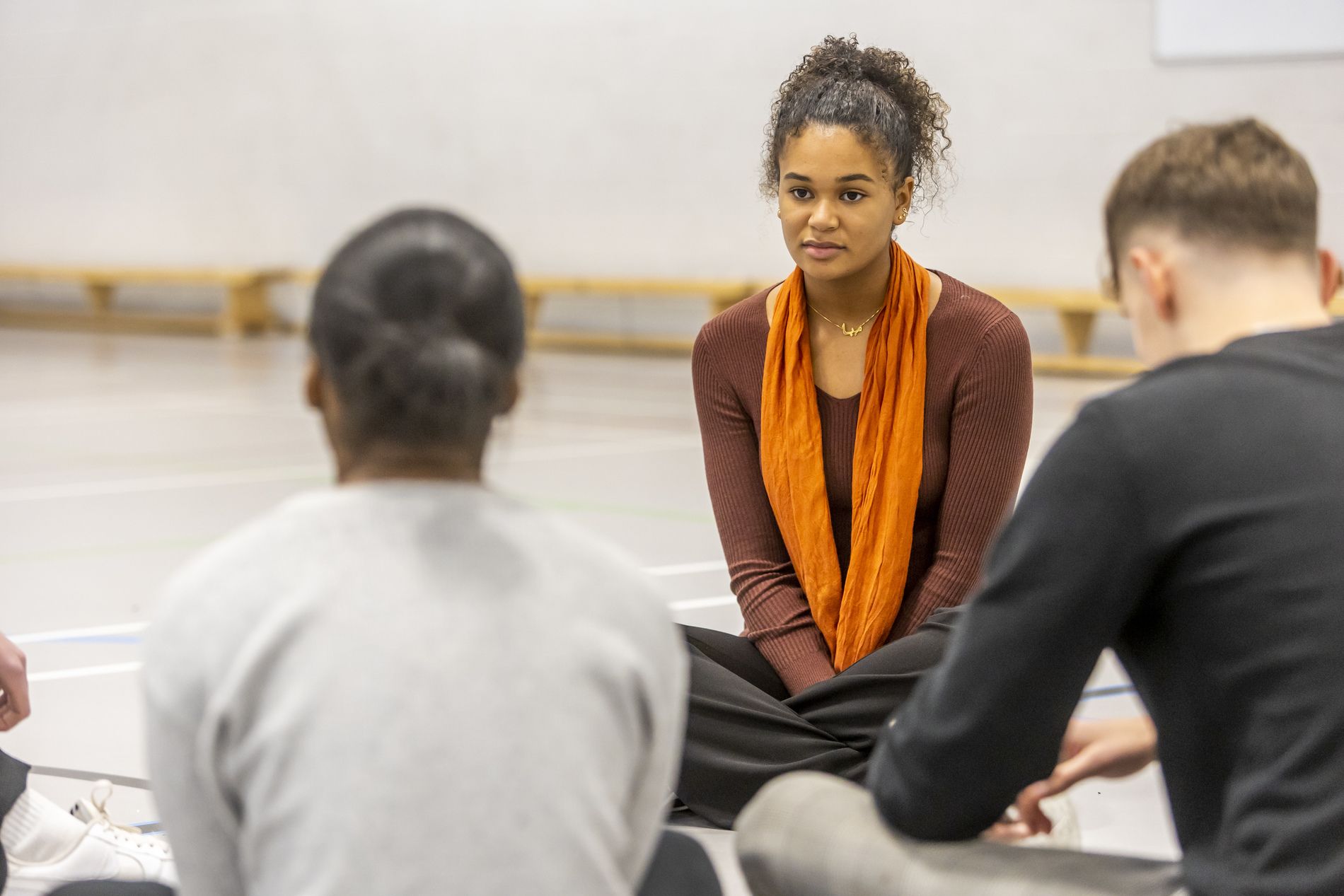 A young woman is sitting on the floor. She is thinking about not wanting to go to university. This is a wide-angle image.