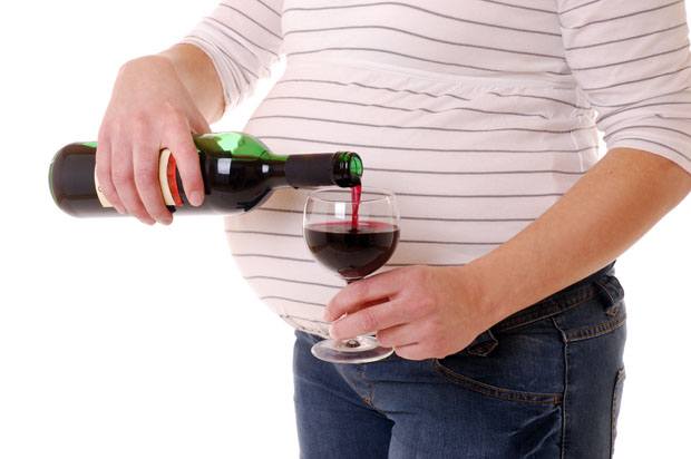 Pregnant woman pouting herself a glass of wine.