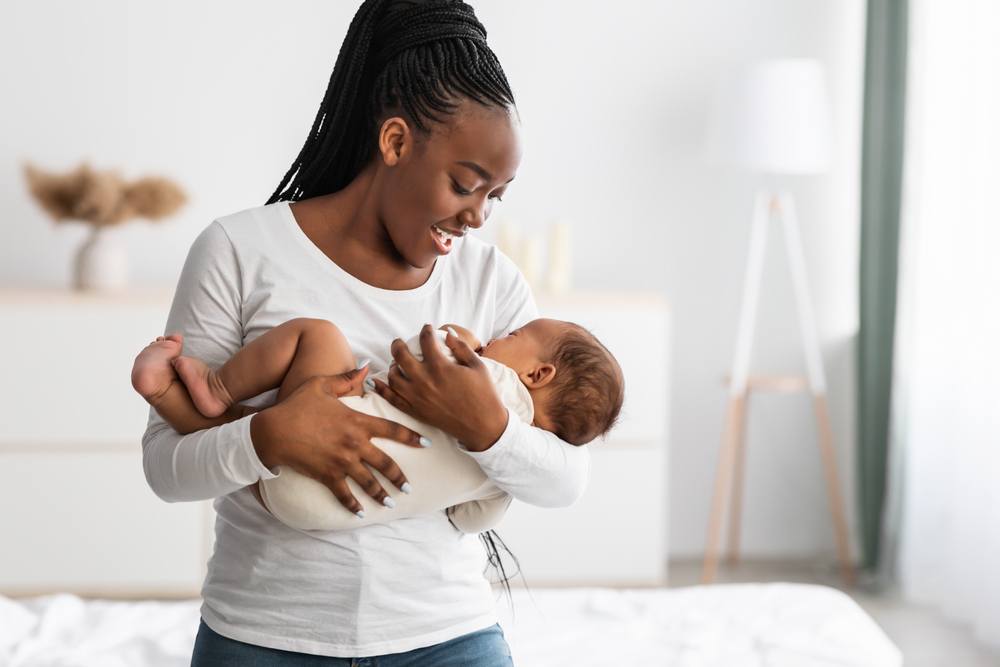 A young woman is holding her child. She is thinking about breastfeeding. This is a wide-angle image.