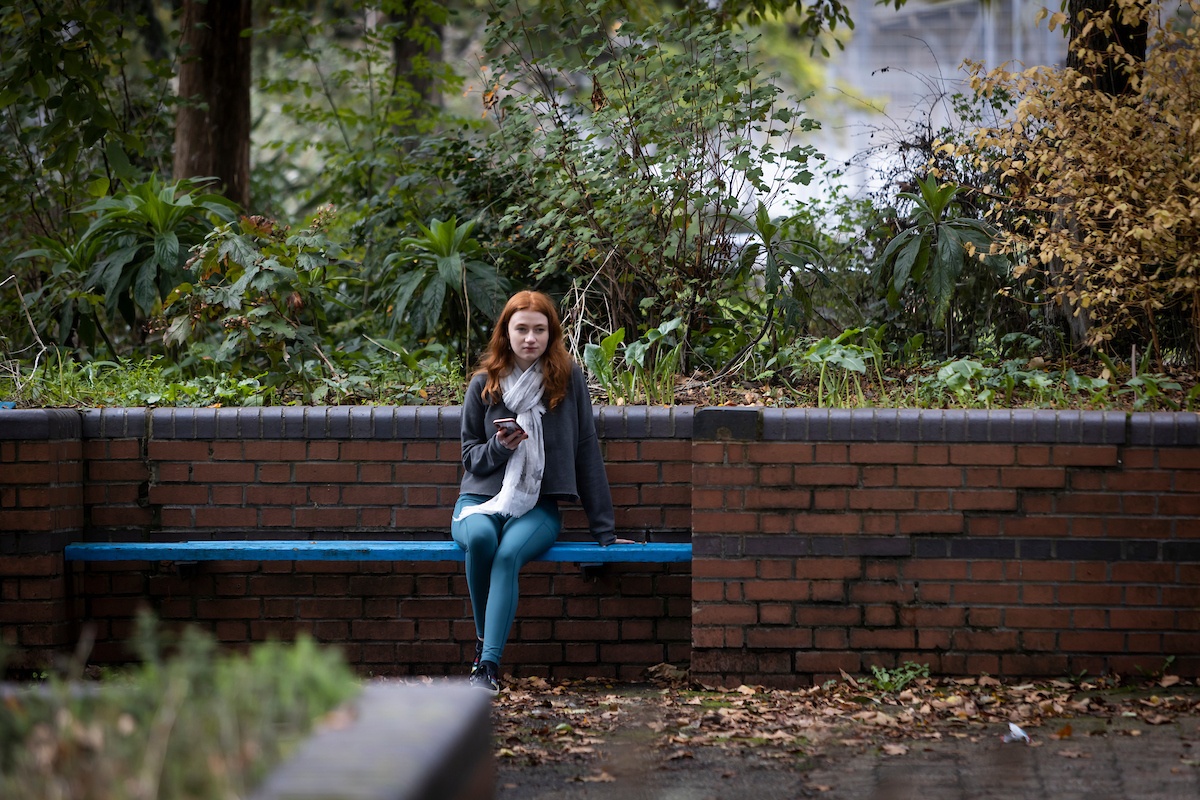 A red-haired young woman is sitting alone on a bench. She has just been caught with drugs. She looks uncertain.