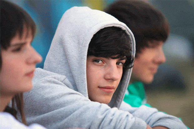 boy in hoody with a slight smile surrounded by two friends