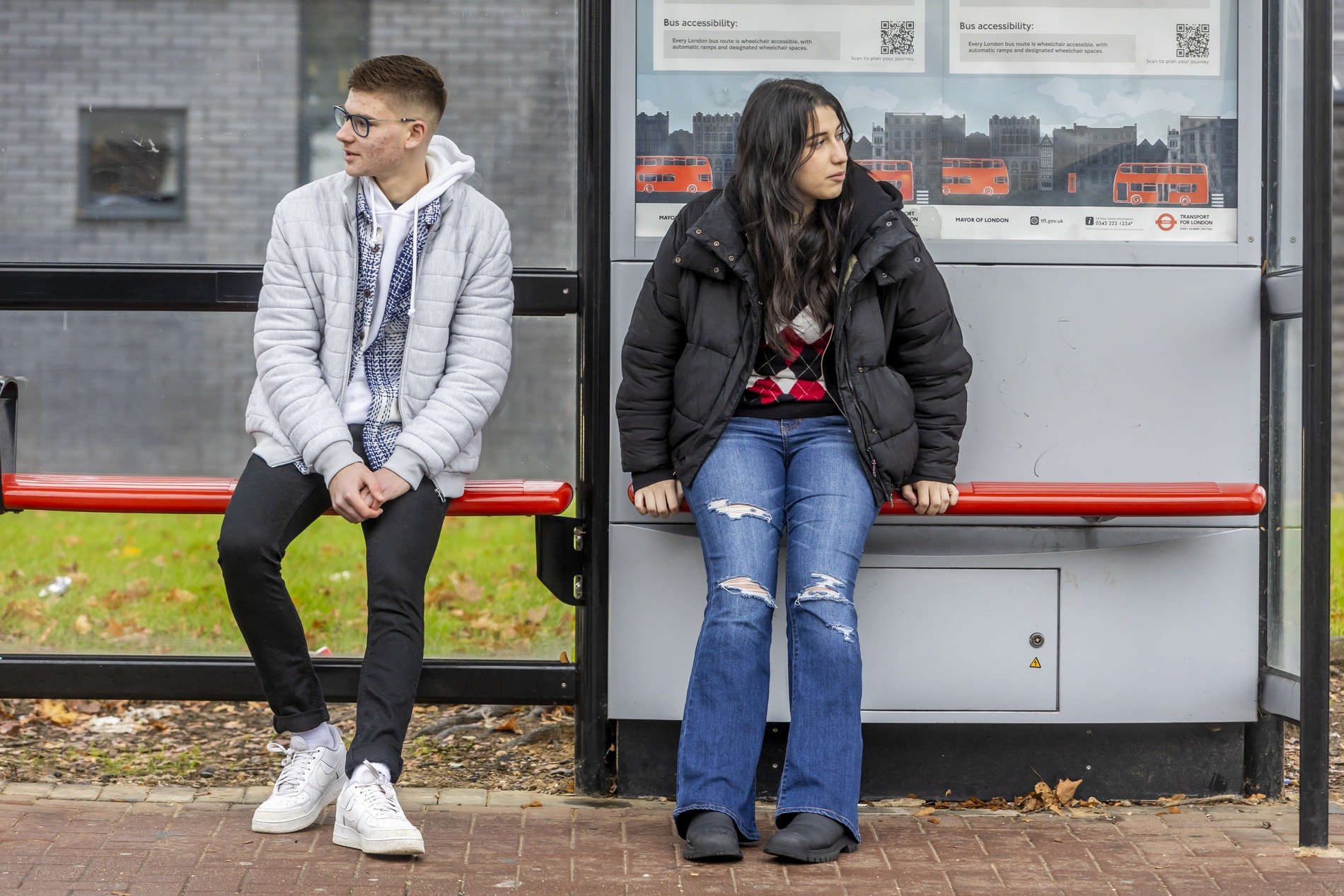 A couple of young people are sitting at a bus stop. They are thinking of flirting.