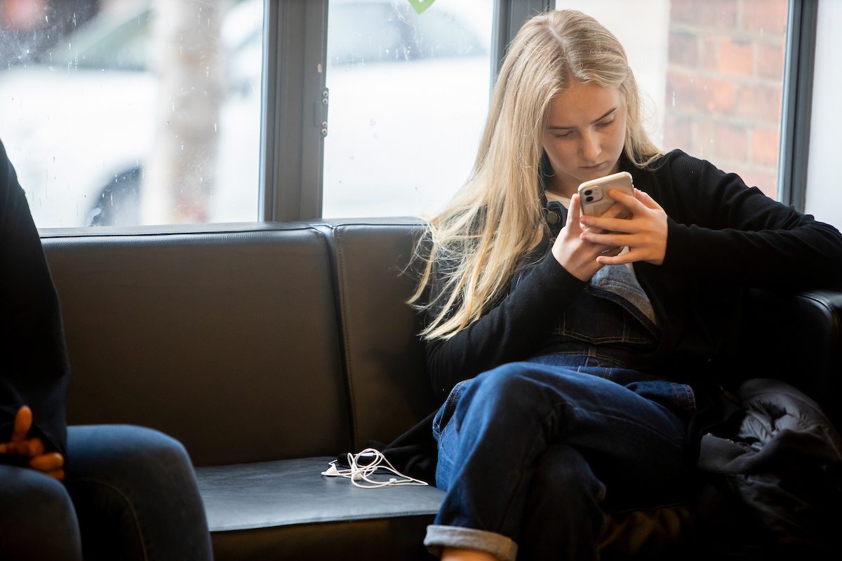 A young woman is on her phone. She is trying to be a good student. This is a wide-angle image.