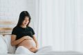 A young pregnant woman is cradling her bump. She is thinking about a healthy pregnancy diet. This is a full-body image.