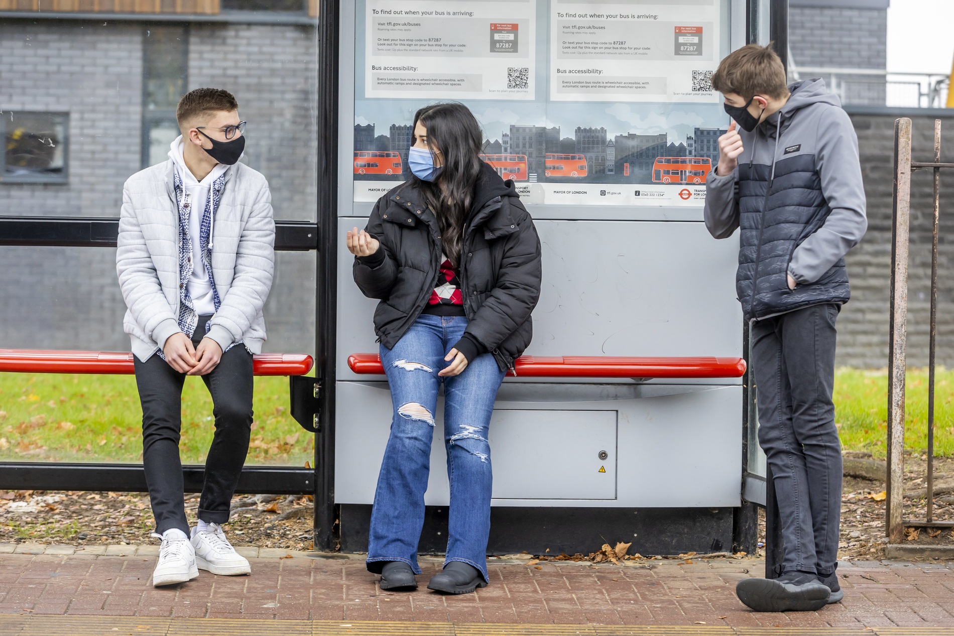 Three young people are waiting for a bus. They are considering volunteering. This is a full-body image.