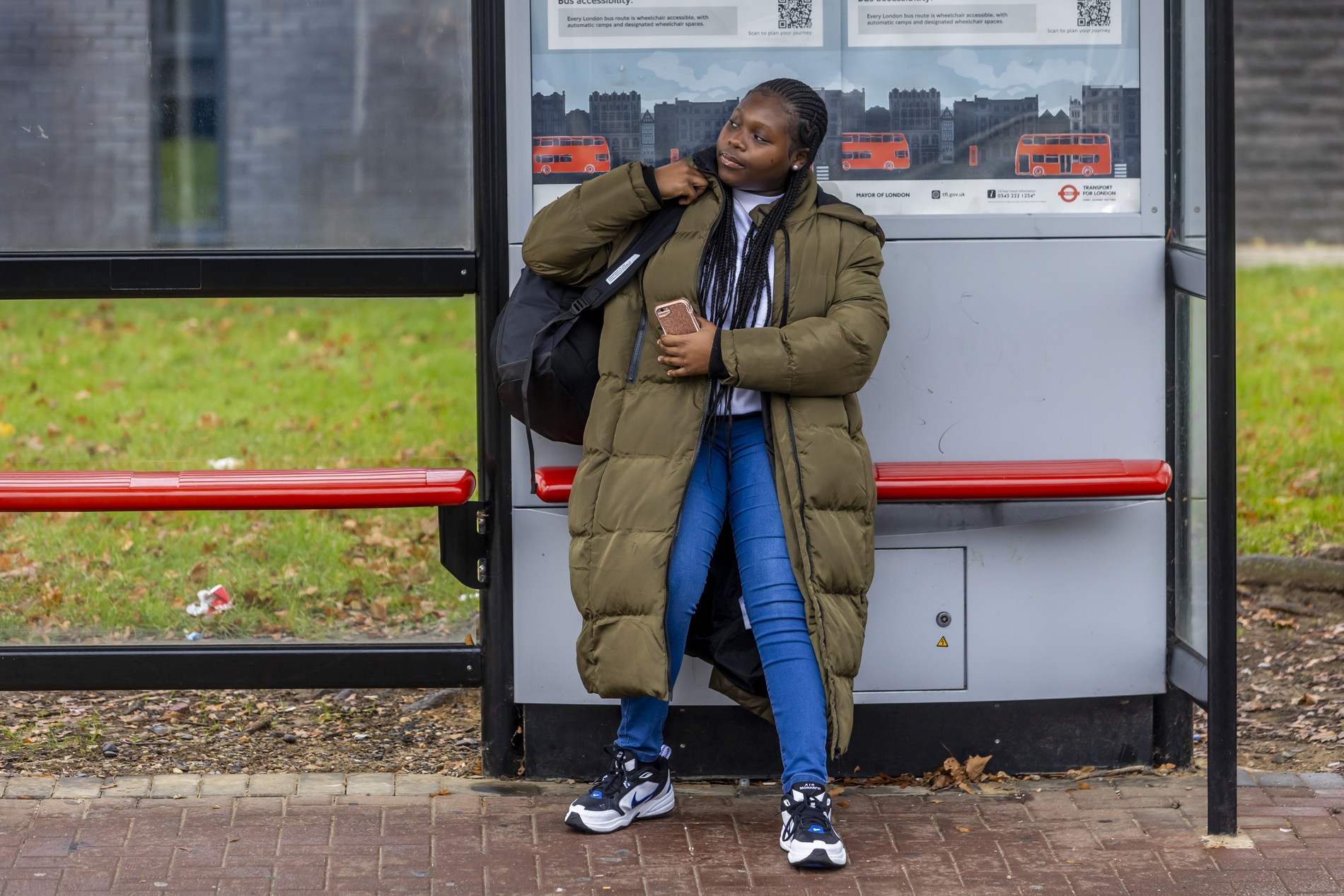 A young woman is standing at a bus stop. She is thinking about being kicked out of her house. This is a full-body image.