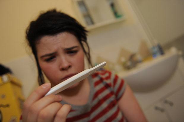 Girl looking worriedly at a pregnancy test