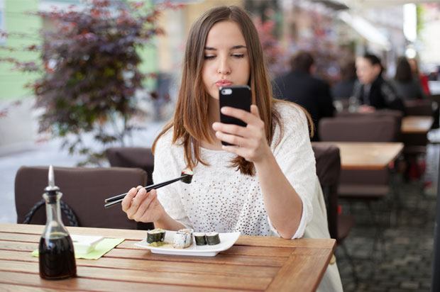 girl sat with sushi looking at her phone