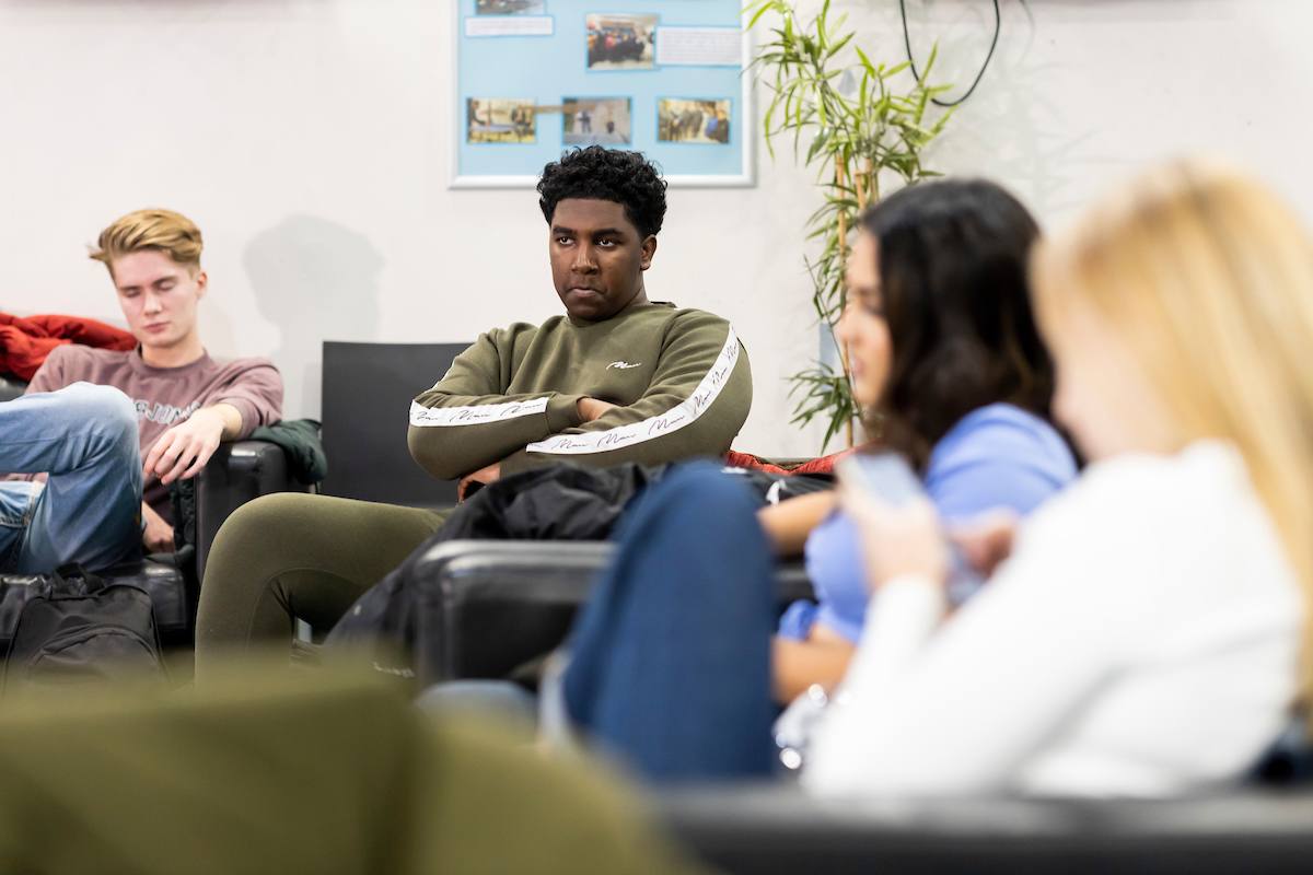 A group of young people are sitting on a sofa. The young man in the middle looks upset. He is thinking about how to say no to drugs. This is a full-body image.