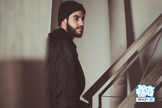 A man with a beard, wearing a black beanie hat and black hoodie