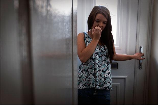 Girl standing at the door biting her fingernails nervously