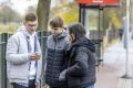 A group of young people are looking at a phone. They are researching unfair dismissal from work. This is a wide-angle image.