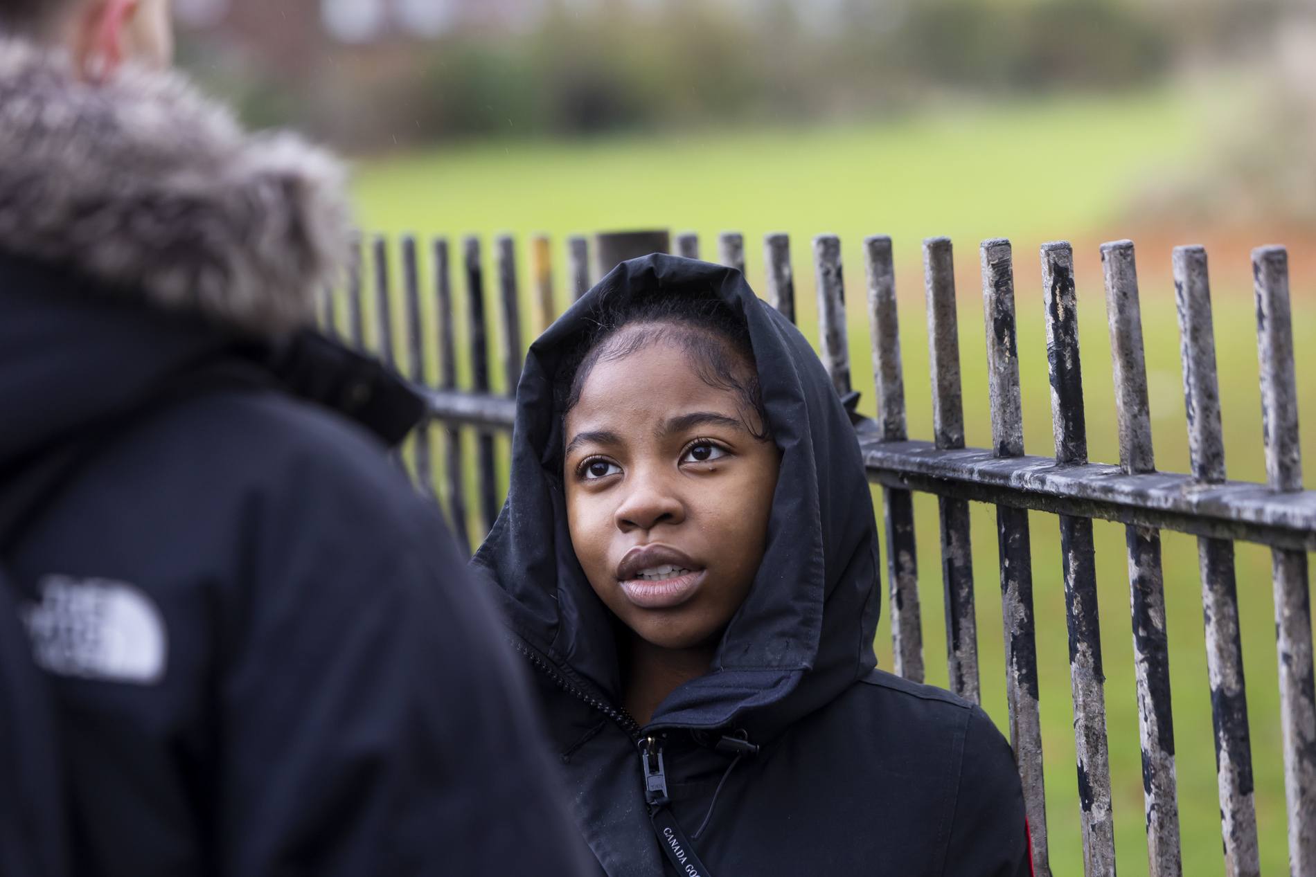 A young woman is leaning on a gate. She is experiencing depression at university. This is a wide-angle image.