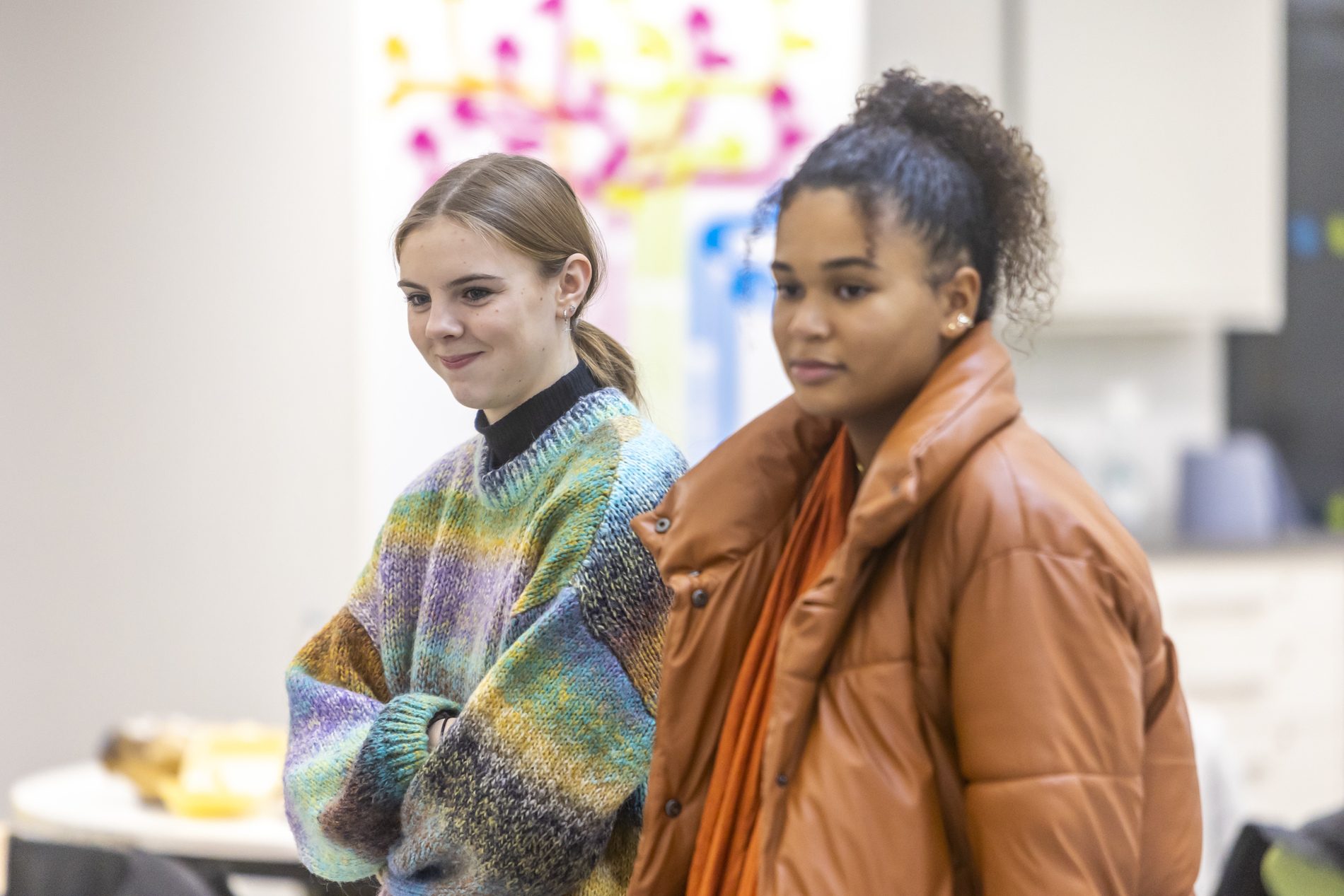 Two young women are thinking. They are wondering about the impact of living with an alcoholic parent. This is a wide-angle image.