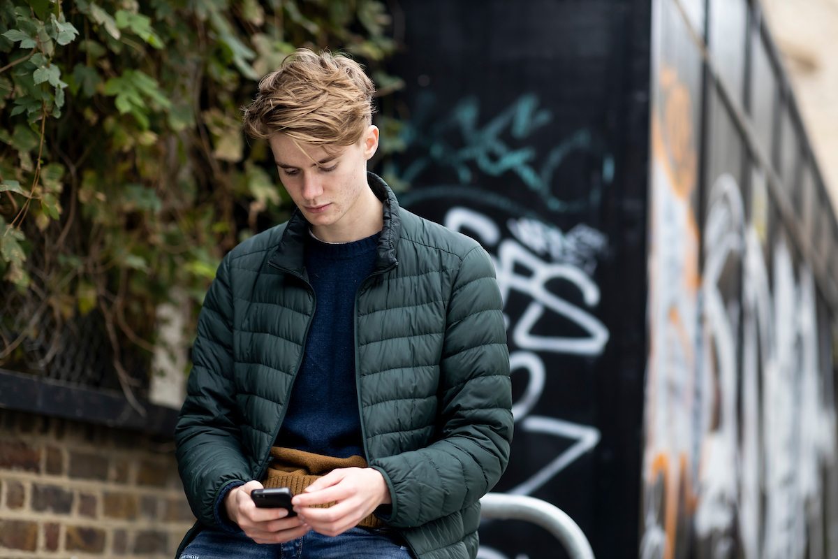A young person is outside looking down at his phone