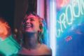 Girl very happy in a club scene with neon lights behind her.