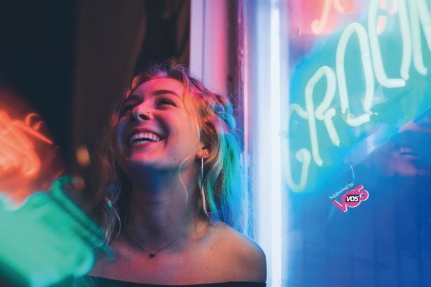 Girl very happy in a club scene with neon lights behind her.