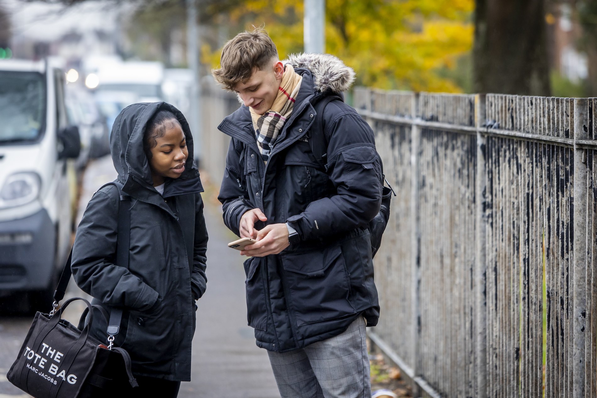 Two young people are standing on the street looking at a phone, talking about stop and search rights.