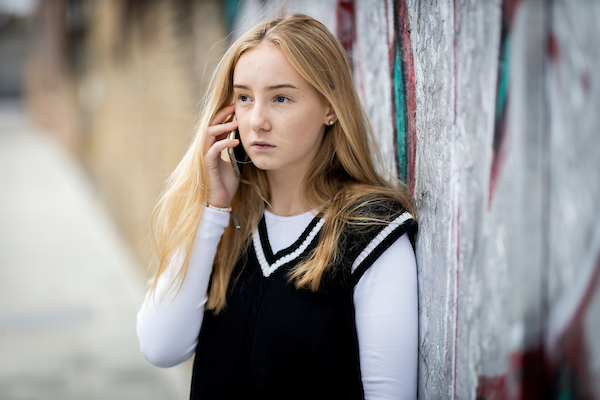 A young women is stood outside on her mobile phone.