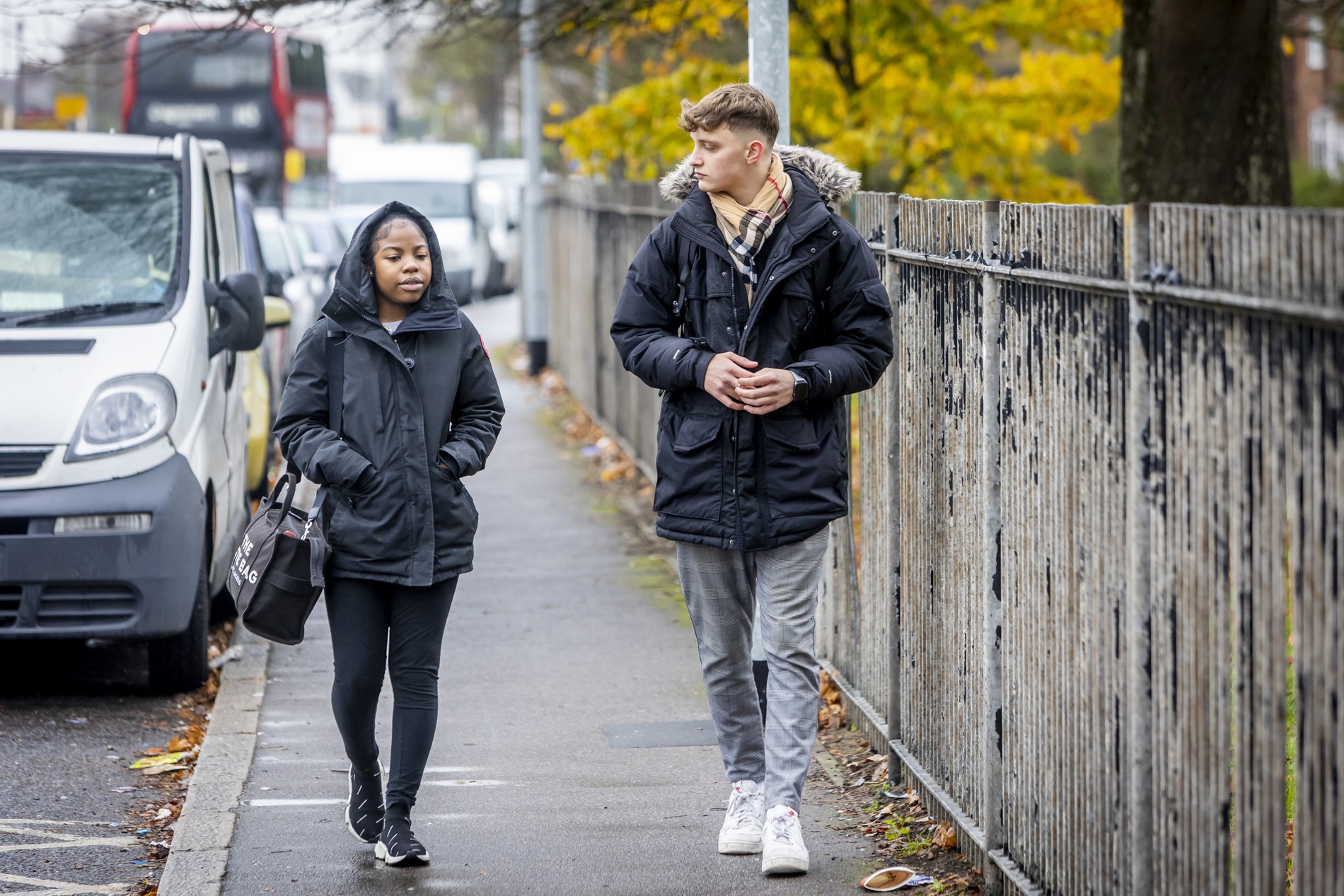 A young couple are walking down the road. They are discussing zero hour contracts. This is a full-body image.