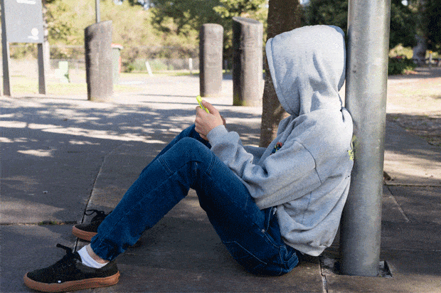 teen guy with hood up sitting on pavement