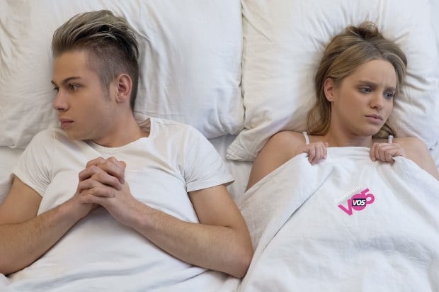A male and female in bed with sheets pulled up to chest looking seperate ways and slightly awkward