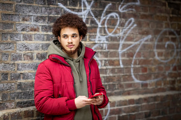 A young person is standing outside against a brick wall thinking about the pressure on guys to sleep around