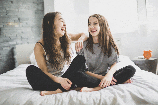 two girls sit on bed laughing
