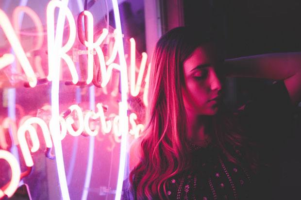 girl closing eyes leaning against pink neon lights