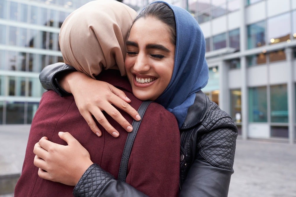Two young Muslim women are hugging. They are discussing be gay and Muslim. This is a wide-angle image.