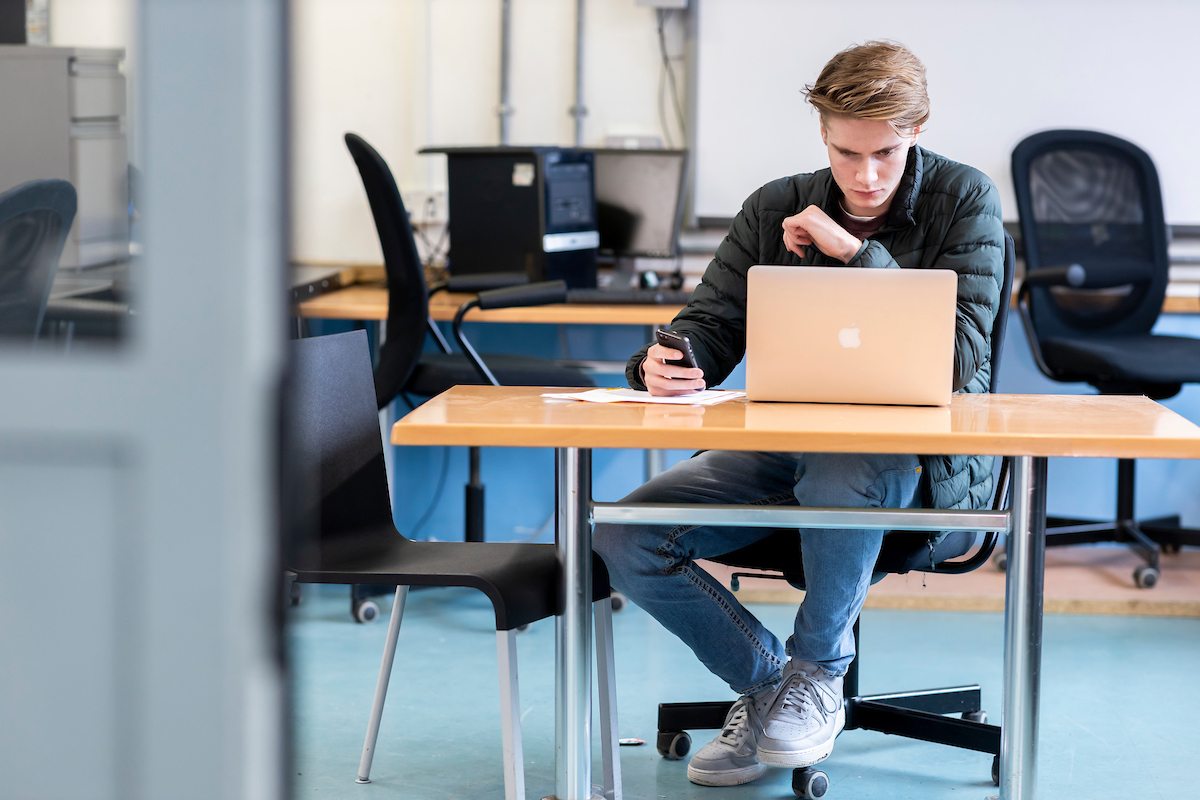 A young man is sitting at a desk. He is experiencing post graduate depression. This is a full-body image.