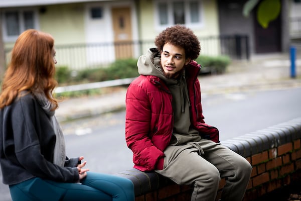 Two young people are sitting on a wall asking the question, what is a man?