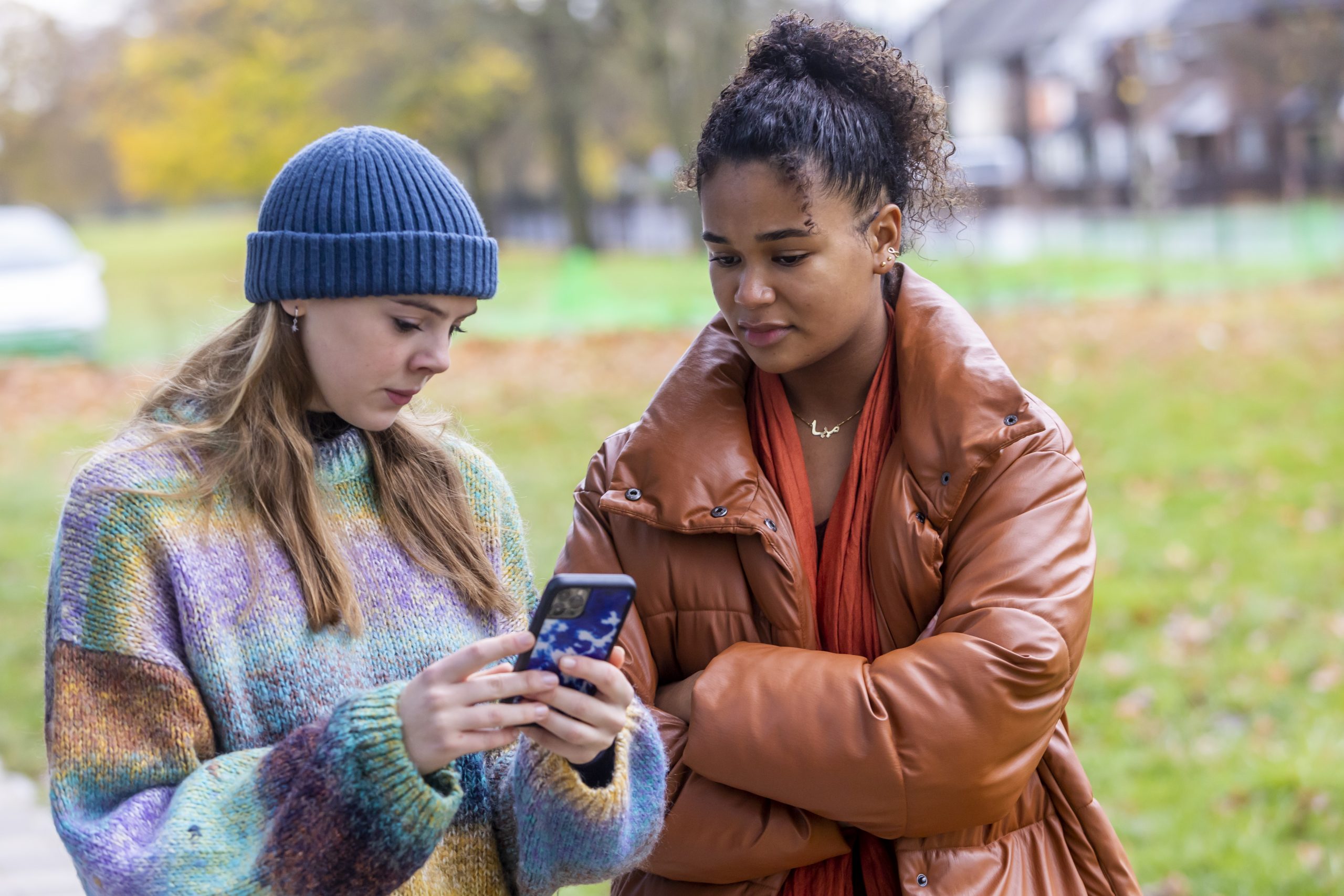 Two young people are standing outside in a field googling "What is labiaplasty?" on a phone