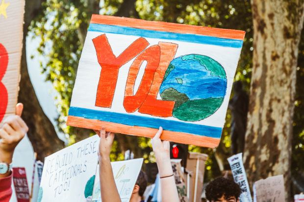 The image shows a poster at the climate strike that states: "YOLO." The "O" is an earth image