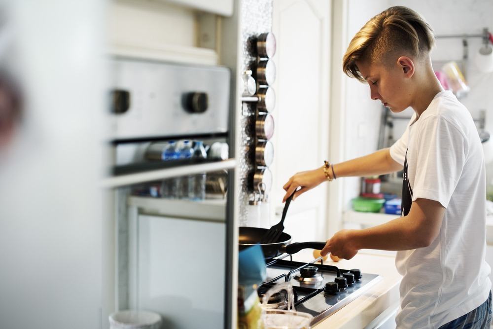 A young person stands in the kitchen cooking