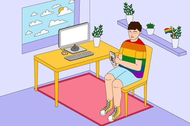 A young person is sitting in their room looking at their phone, wearing a t-shirt with the pride rainbow flag colours.