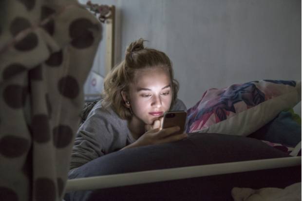A young person is on their phone in their bedroom