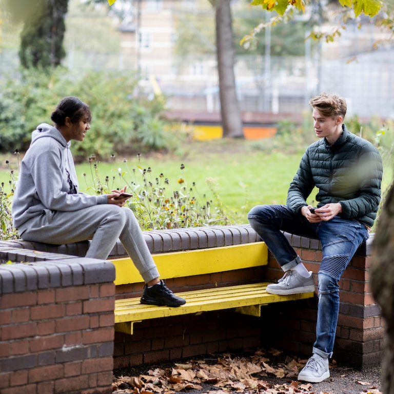Two young people are talking on a bench