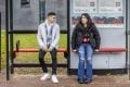 Two young people are sitting at a bus stop talking about leaving prison