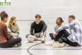 A group of young people sit and chat in a sports hall