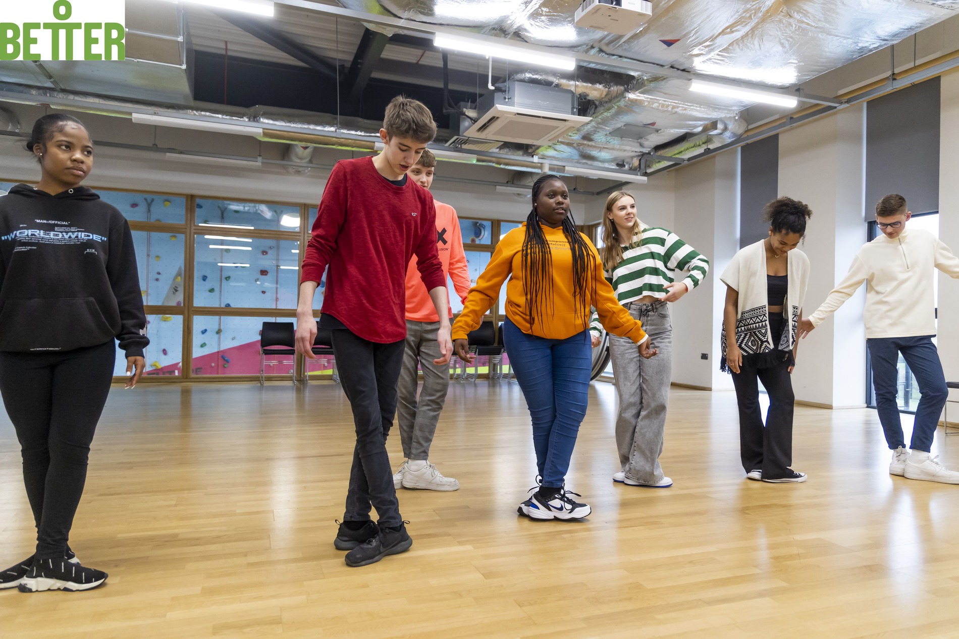 A group of young people practice a dance routine in a sports hall